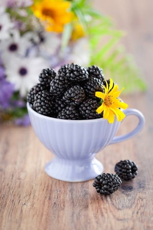 Cup of blackberries and flowers on the table, selective focus の写真素材