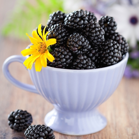 Cup of blackberries and flowers on the table, selective focus の写真素材