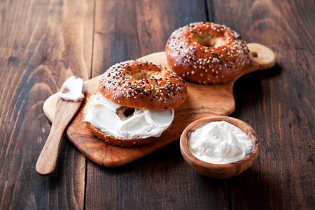 Whole grain bagels with cream cheese on wooden board, selective focusの写真素材