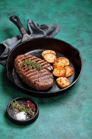 Grilled beef steak and baked potato in cast iron skillet, selective focusの写真素材