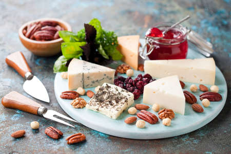 Various types of cheese on a wooden plate with jam, nuts and dried cranberries, selective focusの写真素材