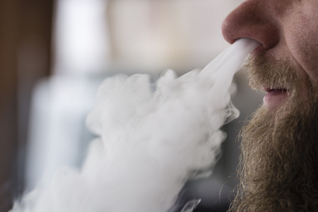 Man with beard and goatee deleted cigarette smoke through the his nose.の写真素材