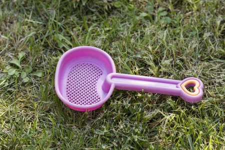 Pink plastic child sieve lying on the lawn - the handle is in the shape of a heart.の写真素材
