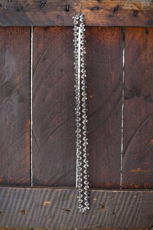 Spare chain for chainsaw hanging with wood in background.
