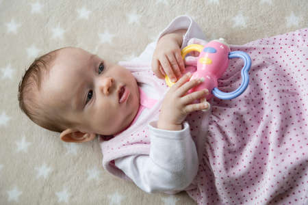 Four month old Caucasian infant lying in a dress on a blanket with stars with a plastic bow tie in...