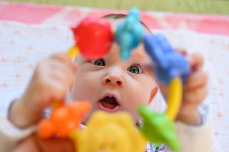 A six month old baby girl with blue eyes lying on her back admires a rattle.の写真素材