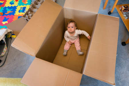 One year old baby girl sitting in a big paper box.の写真素材