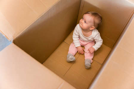 One year old baby girl sitting in a big paper box.の写真素材