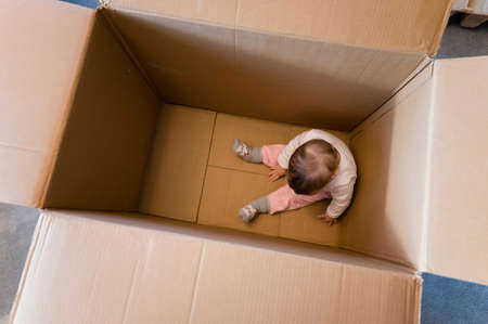 One year old baby girl sitting in a big paper box.