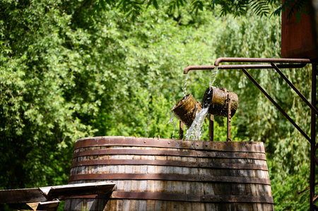 Flipping buckets of water outside by a large barrel.の写真素材