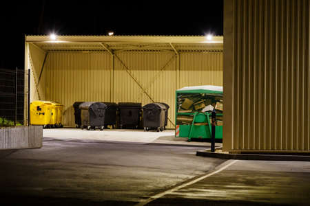 Garbage can for plastic and municipal waste with a paper container under the canopy in the evening.