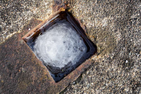 Frozen water in a square hole in the concrete.