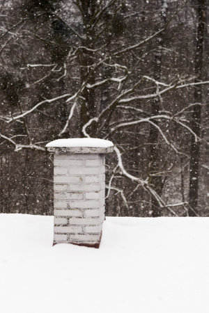 Chimney with snow on the roof with forest in the background.の写真素材