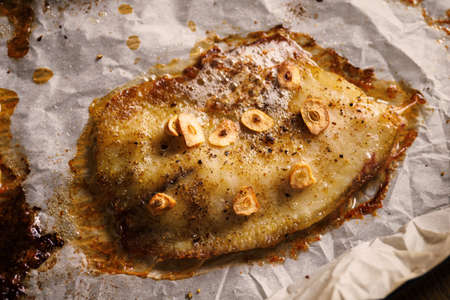 Fish fillet fried in butter and garlic on baking paper.の写真素材