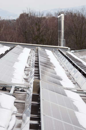 Stainless steel chimney in the background and solar panels on the roof with snow.