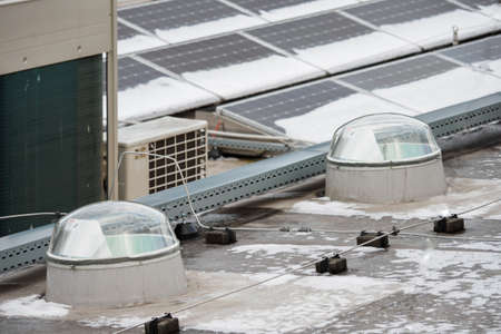 Two domes of light guides on the roof with solar panels with snow.