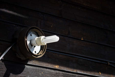 Worn fluorescent light bulb in uncovered light outside on wood.の写真素材