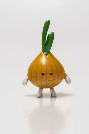 Small figurine of an onion with a growing green stem on a white background.の写真素材