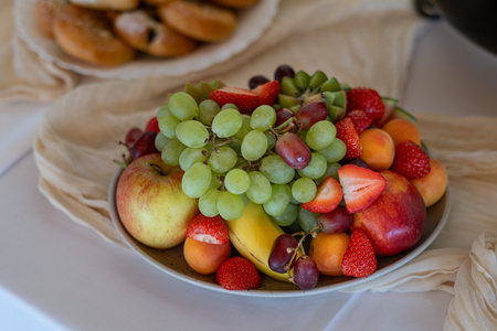 A white plate on the table for guests with fruit - strawberries, apricots, grapes, banana, and apple.の写真素材