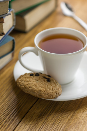 A cup of tea and some chocolate chip cookies over a books on a brown wooden table. Vintage style.の写真素材