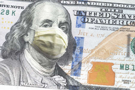 Close up of United States paper currency one hundred dollar bill with Benjamin Franklin wearing yellow doctor mask due to COVID-19 pandemic making a great finance or economic background amidst crisis.の写真素材