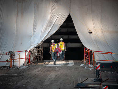 Chicago, IL - March 10th, 2020: Construction workers pass through the tented and tarped facade of...