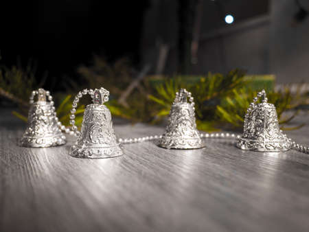 A closeup photograph of silver Christmas bells on a beaded strand on a gray woodgrained floor and...