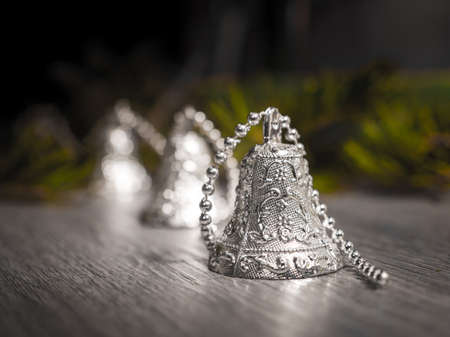 A closeup photograph of silver Christmas bells on a beaded strand on a gray woodgrained floor and...