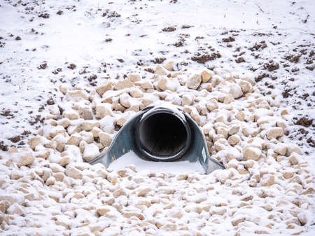 A closeup view of a large storm water drainage culvert pipe emptying into a retention pond set in...