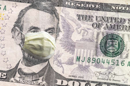 Close up of United States paper currency five dollar bill with Abraham Lincoln wearing yellow doctors mask due to  pandemic making a great finance or economic background amidst the crisis.の写真素材