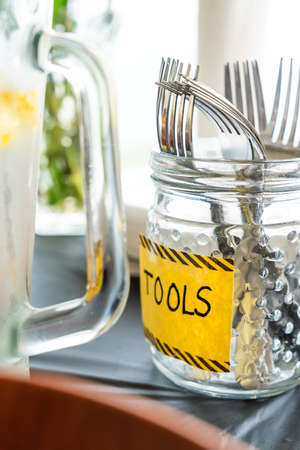 A close up photograph of forks in a textured glass mason jar on black table cloth with the word...