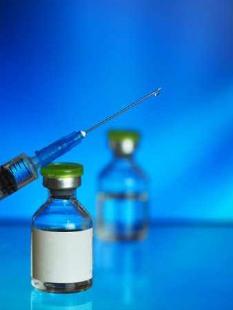 drop of transparent vaccine on the tip of a needle syringe, glass vials, blue background, a vertical image with a soft focus, a wide banner, a place for textの写真素材
