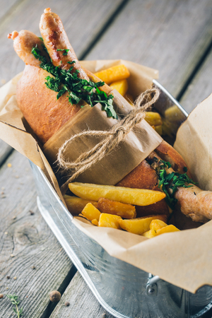 Hot Dog with French Fries wrapped in Paper and tied by twine in Bowl on wood backgroundの写真素材