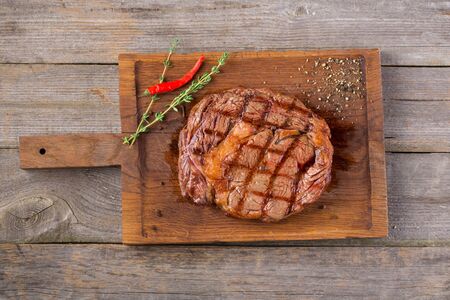 Rib eye steak on wooden board, closeup. Rib eye steak on wooden board decorated with chili pepper and thymeの写真素材
