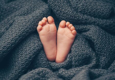 Soft newborn baby feet against a dark grey blanket, closeup.の写真素材