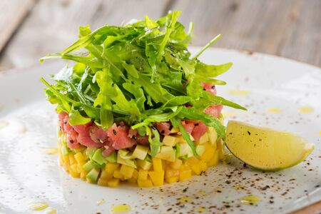 Delicious avocado, mango and raw salmon salad, tartare, served on a white plate with limeの写真素材