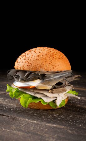 Fresh tasty burger with plastic waste inside on dark wooden background. Plastic pollutionの写真素材