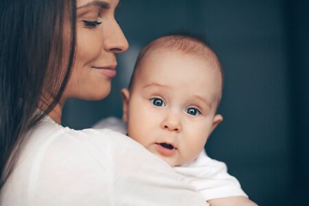 Close-up portrait of a serene cute beautiful baby boy on hands of happy smiling mother. Healthcare and medical love woman mothers day concept.の写真素材