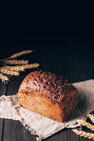 Loaf of black bread on textile towel on dark wooden table on black background with copy space