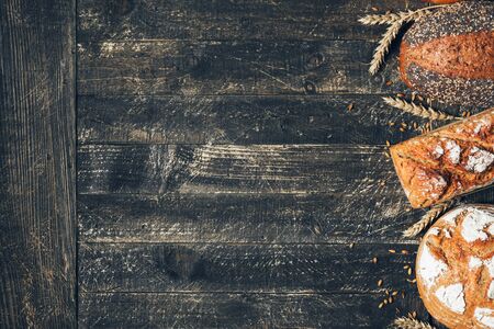 Brown and white breads with spikelets on wooden background with copy space. Three different types of bread. Bakery, cooking and grocery store conceptの写真素材