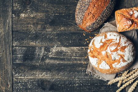Brown and white breads with spikelets on wooden background with copy space. Three different types of...