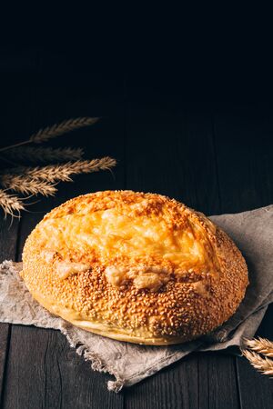 Loaf of white bread with cheese on textile towel on black wooden background with copy space
