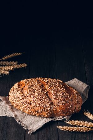 Loaf of brown bread with sesame and linseeds on textile towel on black wooden background with copy spaceの写真素材