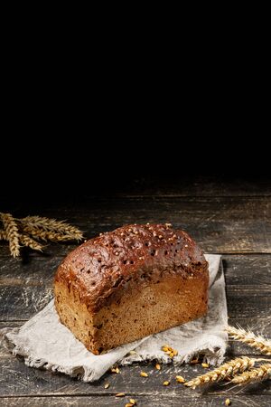 Loaf of black bread with seeds on textile towel on rustic wooden texture background. Vertical...