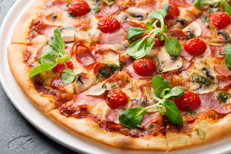 Sliced tasty pizza with mushroom, cheese, tomatoes, pepper, becon, sausage, fresh salad and pesto. Italian pizzaの写真素材