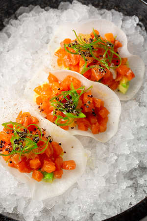 A modern serving of salmon and avocado tartare served in rice chips on ice crumbs.の写真素材