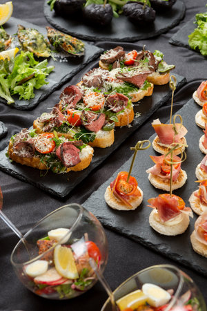 Festive appetizer. A set of bruschetta with roasted beef, cherry tomatoes and grated cheese, as well as toasted canapes with bacon, cherry tomatoes and cream cheeseの写真素材