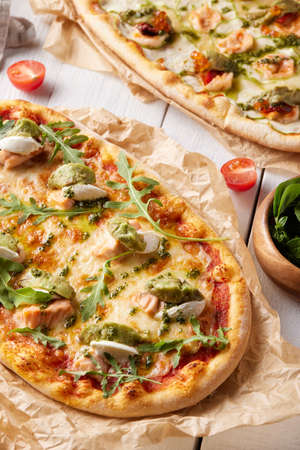 Set of tasty pizzas with fish, broccoli, mozzarella and arugula on parchment paperの写真素材