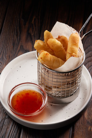 Basket of breaded cheese sticks with ketchup on white plate on wooden table