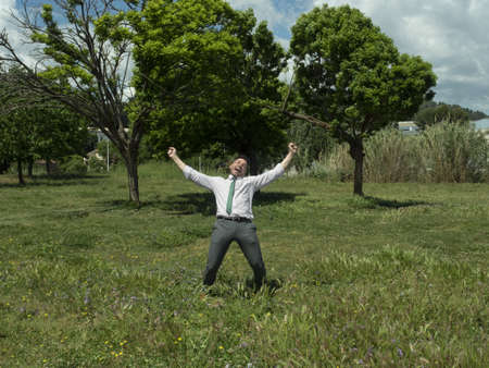 a green park with trees a businessman with a positive attitude is celebrating with open arms and a very happy face.の写真素材